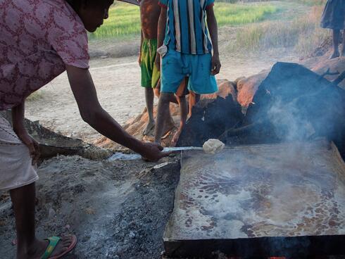 A person cooks food over a stove outdoors