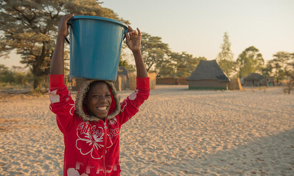 Smiling woman holding bucket on her head