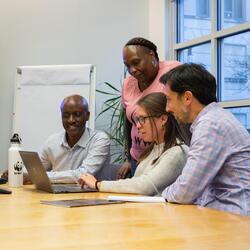 Four WWF-US staff--a Black man, a Black woman, a man with dark hair and a short beard, and a woman with brown hair--surround a laptop in a conference room. 