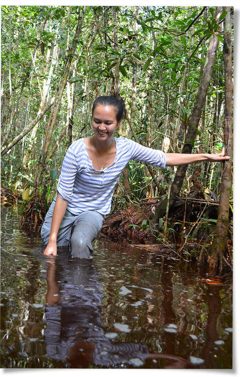 Stephanie Roe stands in wetland, leaning on tree