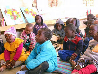 Young students sit on the ground paying attention to a lesson