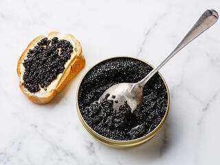 Sturgeon black caviar in can and slice of toast on white marble background