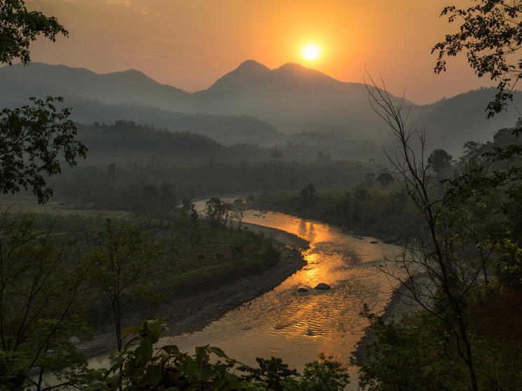 A lush landscape in Nepal with mountains in the background and a winding river at sunrise