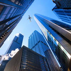 Looking up, between tall buildings at an airplane flying above