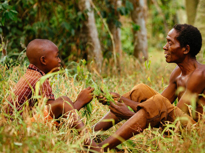 Man and boy sit facing one another in forest