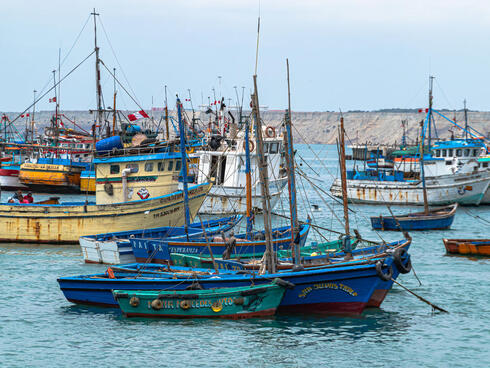 A cluster of small Peruvian fishing boats colored blue, green, yellow, and white that are moored in a secluded harbor on a hazy day.