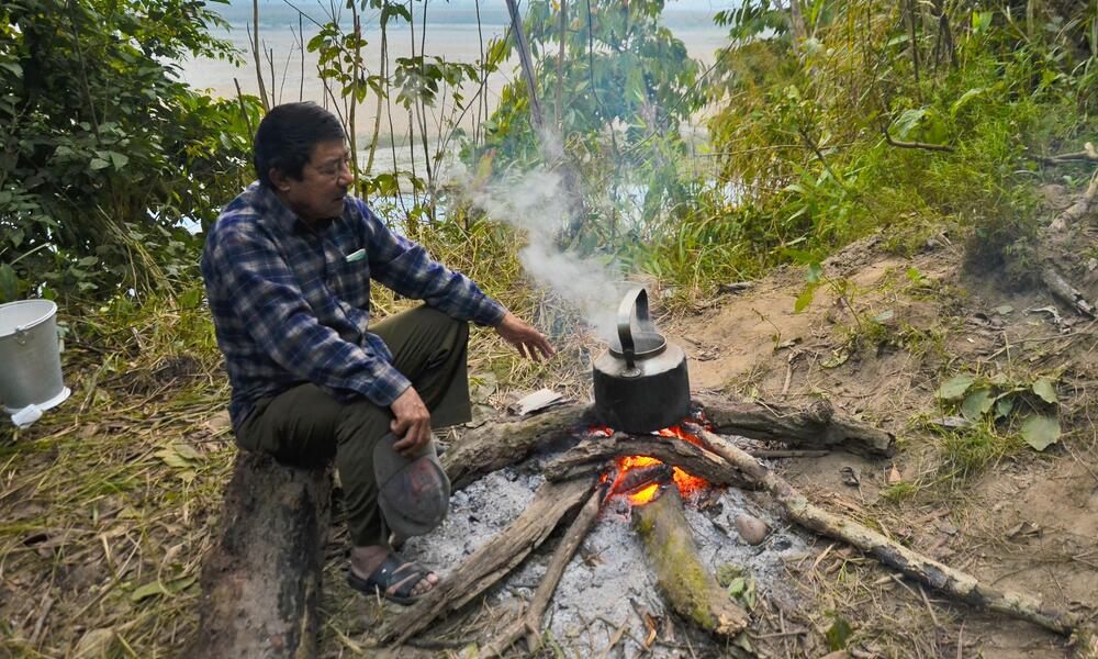 A man sits at a campfire in the woods cooking something over the flames