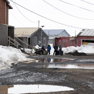 People gather around UTVs near a red building in town