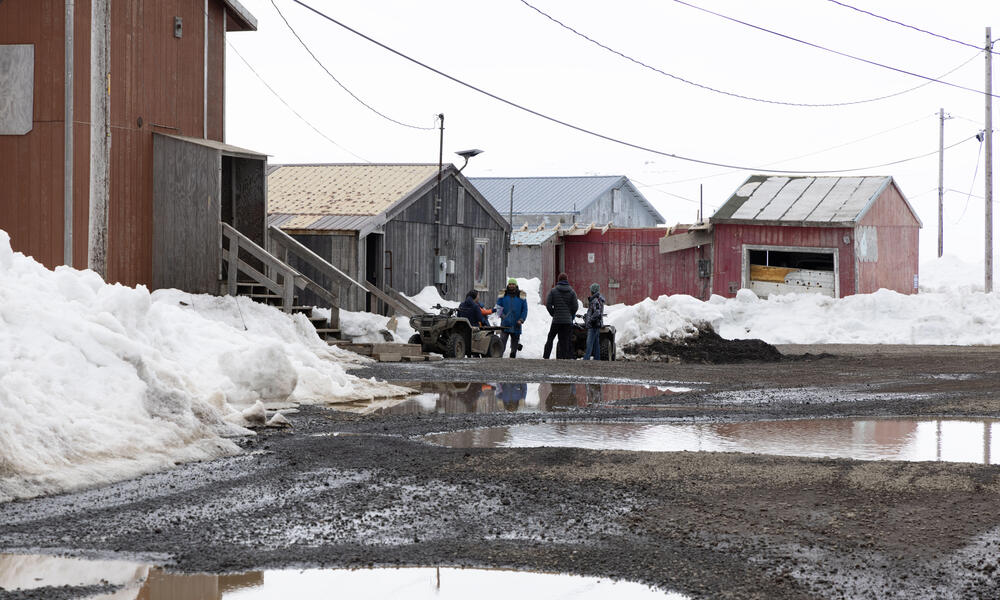 People gather around UTVs near a red building in town