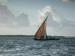 In the evening, a fishing boat with a single triangle sail sets out on the water