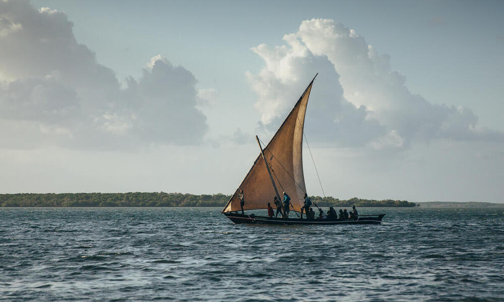 In the evening, a fishing boat with a single triangle sail sets out on the water