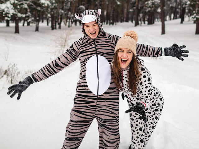 Two adults wear animal onesies and pose in a snowy environment