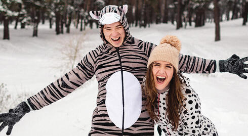 Two smiling adults wearing onesies on the snow