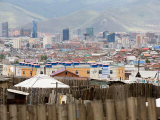 Landscape view of a city against a mountainous backdrop with a wooden fence in the foreground