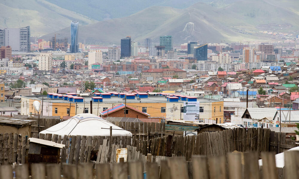 Landscape view of a city against a mountainous backdrop with a wooden fence in the foreground