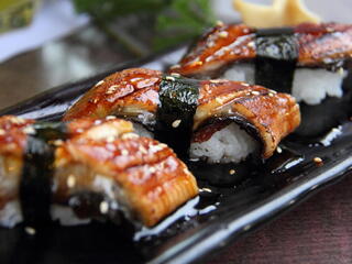 Three pieces of unagi sushi on a black platter