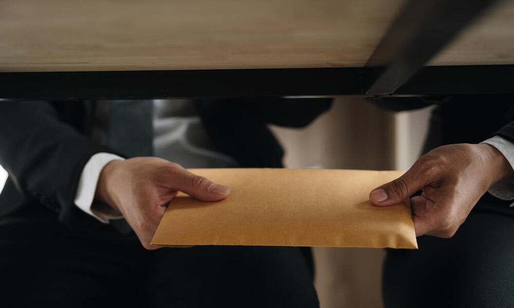 Two hands passing an envelope under table
