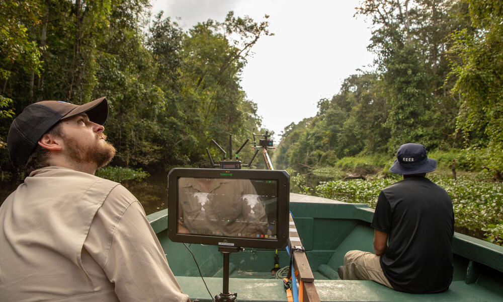 A behind-the-scenes photo of two team members in a boat going through the Bornean rainforest. 