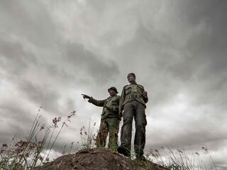 Two village game scouts stand on a rock and look over the landscape.