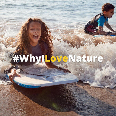 A girl on a body board laughs as she catches a wave in the sun