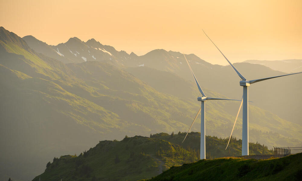 Two wind turbines on a mountain in Alaska with a setting sun and mountains in the background