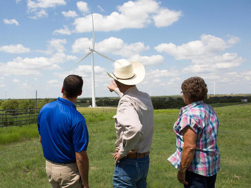 People talking in a field while pointing to a wind turbine