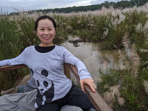 Winnie Lam smiles at the camera as rhinos play in the water behind her