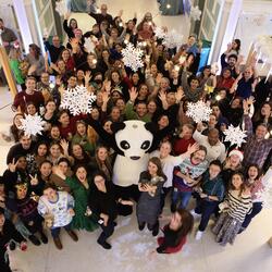 WWF-US staff gather around Pandy the mascot and pose for a photo at the winter staff party. The atmosphere is festive and warm.