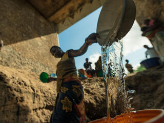 A woman filling up a bucket of water at a makeshift well under a bridge