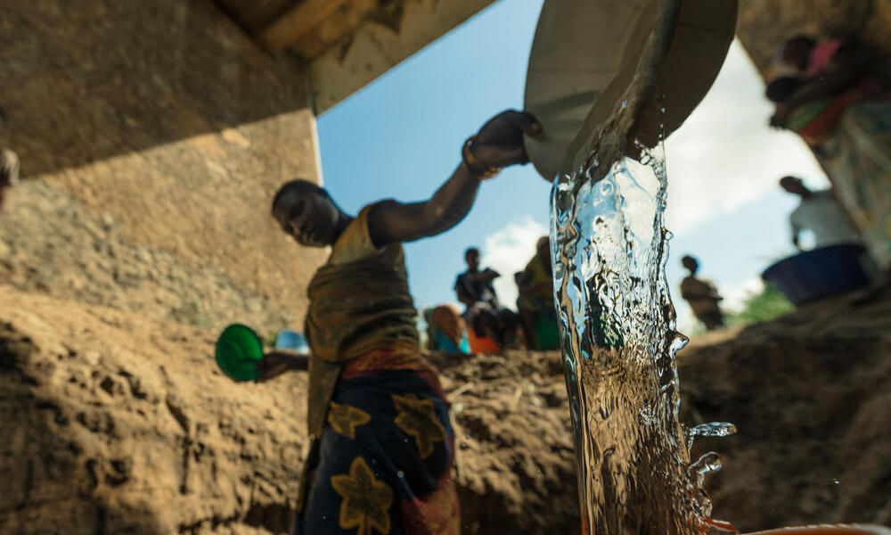 A woman filling up a bucket of water at a makeshift well under a bridge
