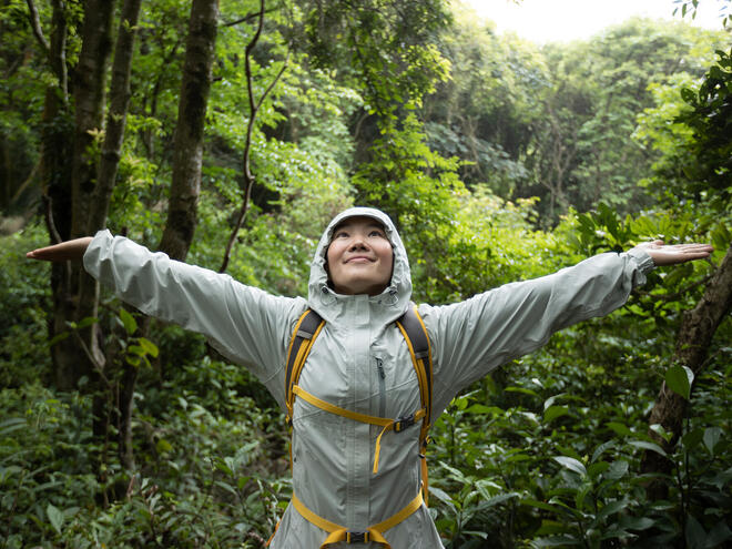 Smiling woman standing in forest with arms spread