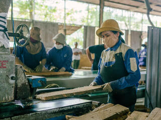 A woman in a mask and gloves feeds a board into a machine