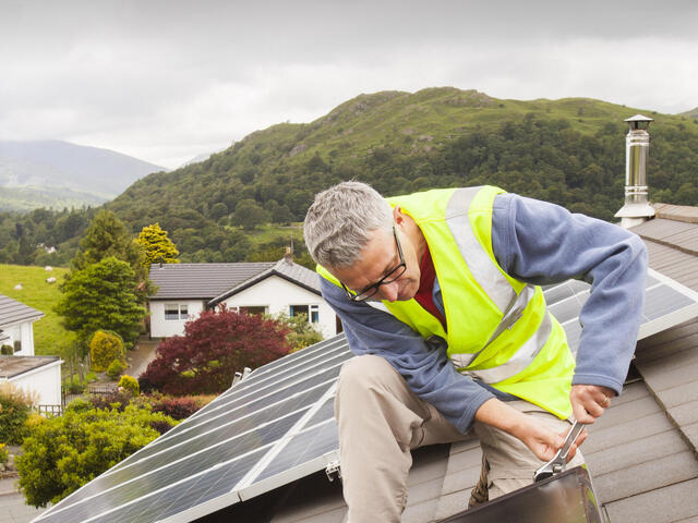 A workman fitting solar thermal panels for heating water, to a house roof in Ambleside, Cumbria, UK, that already has solar PV for generating electricity.