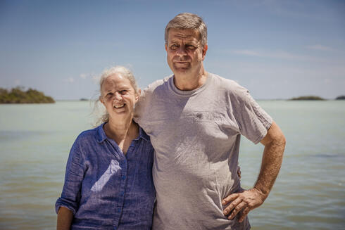 Zoe and Paul Walker stand in front of a blue lagoon on a bright day in Belize