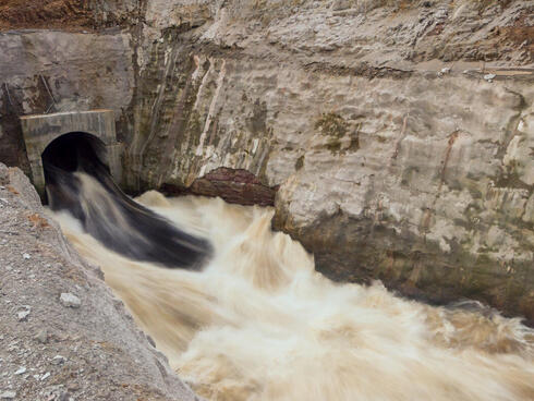 Water rushes through a tunnel in a hydropower dam with brown rock nearby