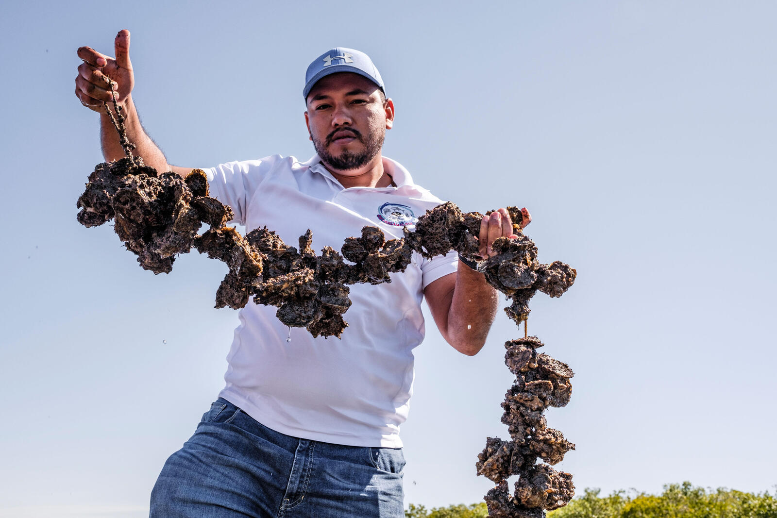 Pedro Alfonso Lopez Gonzalez holds a string of oysters on a sunny day
