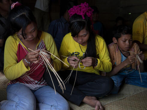 Two women and a small boy sit on the floor weaving crafts