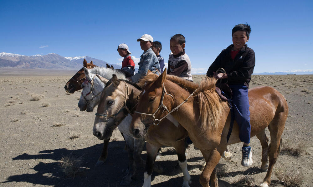 A group of people on horseback in a row smile and look at the camera