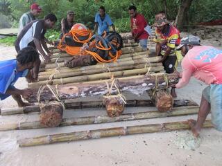a group of men build a raft on the sand out of wood, bamboo, and rope
