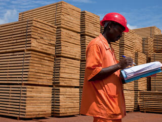 A man checks paperwork in front of stacks of lumber