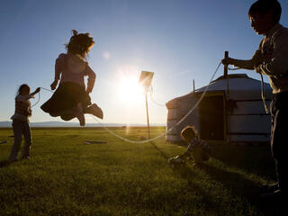 Three children jumping rope on the grass in the sunset