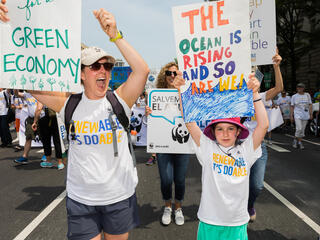 people hold up signs that read "green economy" and "the ocean is rising and so are we"