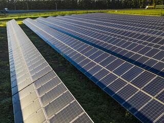several rows of solar panels amid soil and green grass