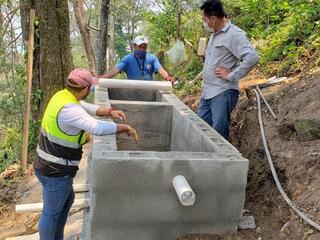 A group of Honduran men in a forest surrounded by bags of concrete and other materials to build a new water system 