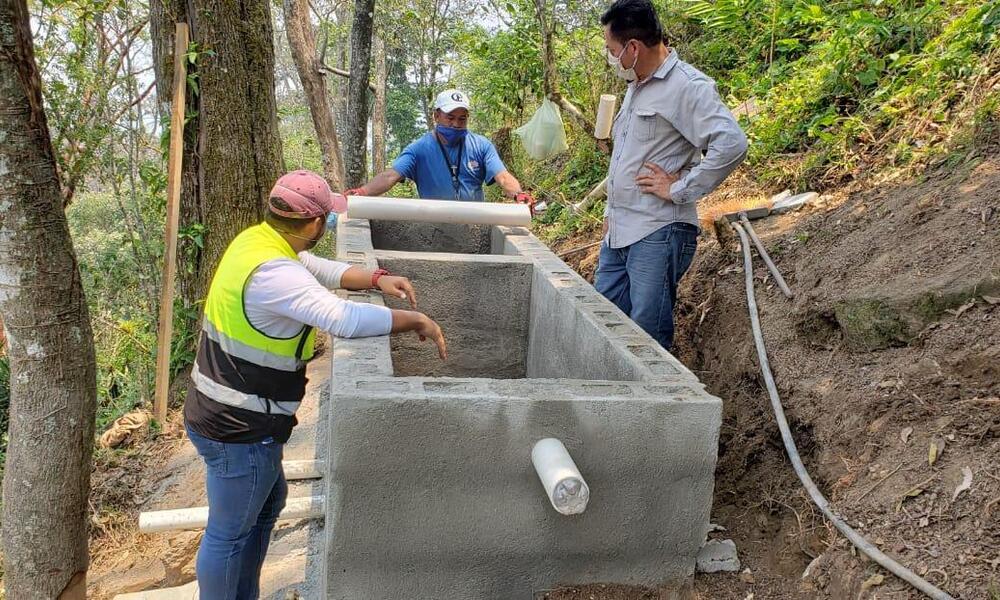 Three men stand around a cement structure in the forest while building a new water system