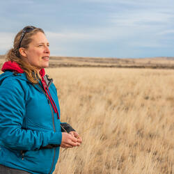 A woman stands in a field of brown grass
