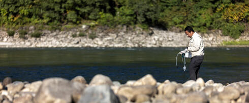 A man stands beside a river holding testing equipment