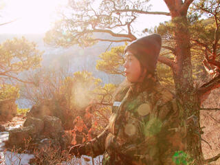 A female ranger prepares to begin her day, standing against a forest backdrop as the sun rises