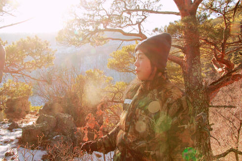 A female ranger prepares to begin her day, standing against a forest backdrop as the sun rises