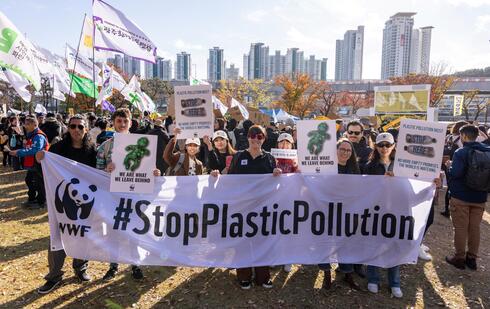A group of people marching outdoors behind a banner that reads "#StopPlasticPollution"